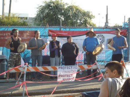 Musqueam drummers outside fence of construction site.