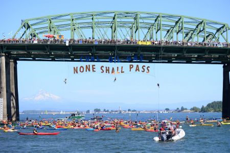 Rising Tide repelled off a bridge in Washington State to oppose an approved oil export terminal. Banner says, “Coal, Oil, Gas. None Shall Pass.”
